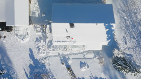 Drohnenaufnahme-Von-Oben-Nach-Unten,-Die-über-Einer-Teilweise-Gereinigten-PV-Anlage-Auf-Einem-Schneebedeckten-Hausdach-Aufsteigt