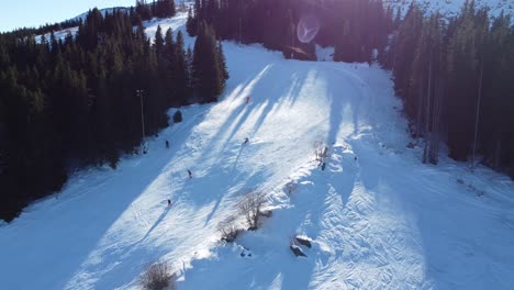 Static-aerial-clip-of-people-skiing-round-the-bend-of-a-mountain-slope-in-the-sunshine-at-Vitosha-ski-resort-near-Sofia,-Bulgaria-with-a-chairlift-running-in-the-background
