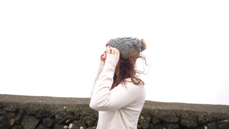 Profile-shot-of-woman-on-a-windy-day-adjusting-beanie-in-Azores-by-sea-wall
