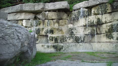 Low-Pull-Out-Panning-Shot-of-a-Waterfall-in-a-Garden-with-Decorative-Stone-Wall