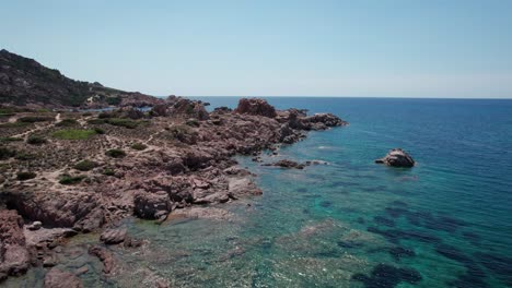 aerial-footage-traveling,-tilt-up-shot-on-rocky-coastline-in-Sardinia-island,-Italy-during-summertime,-travel-destination