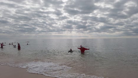 Eine-Mutter-Und-Eine-Tochter-Kommen-Im-Dezember-Beim-Weihnachtsmannschwimmen-In-Rot-Aus-Dem-Meer