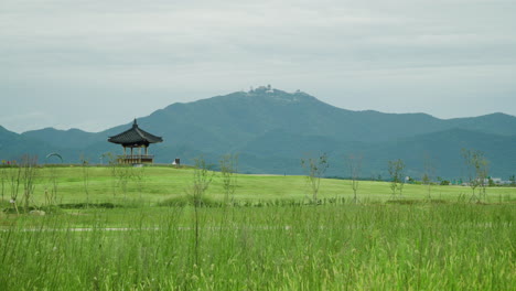Pagoda-Tradicional-Coreana-En-Una-Colina-Verde-Cubierta-De-Hierba-Contra-Majestuosas-Montañas-En-El-Parque-Nacional-Del-Complejo-Ecológico-Saemangeum---Panorámica
