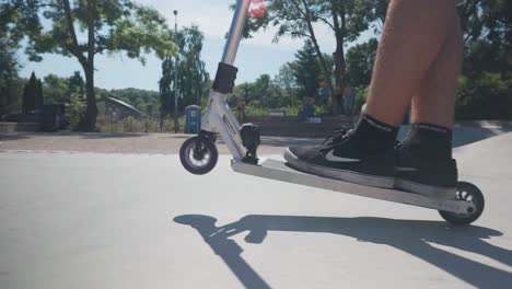 Man-on-silver-color-stunt-scooter-perform-wheelie-on-concrete-skatepark-ground