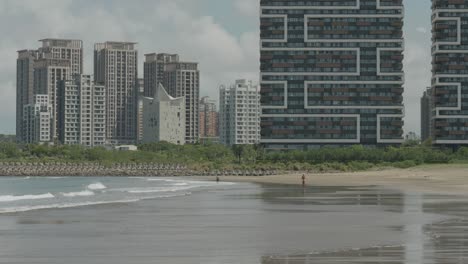 Ocean-water-spreads-across-sandy-flats-of-Shalun-beach-with-skyscrapers-behind