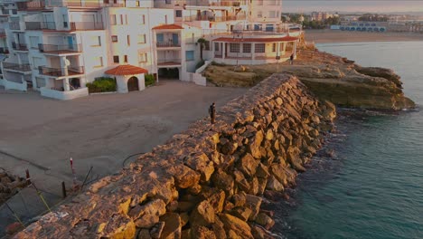 Tourist-standing-on-rocky-pier-at-golden-hour-in-Roc-de-Sant-Gaieta-Village
