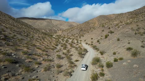 View-above-white-car-off-roading-in-desert-hills,-aerial-view