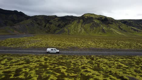 Road-trip-on-gravel-road-of-Iceland-with-mountain-background,-aerial-follow-shot