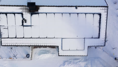 Aerial-top-down-shot-rising-above-solar-cells-on-a-melting-house-roof,-winter-day
