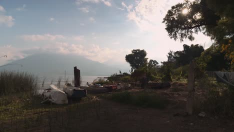 Small-boats-on-shore-of-Lake-Atitlan-at-sunrise-with-cloud-covered-volcano-in-background