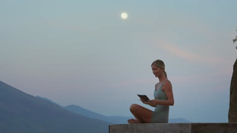 Woman-sitting-in-easy-pose-looking-at-full-moon-and-writing-mental-note-in-journal