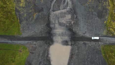 White-van-crossing-muddy-river-in-Iceland-travels,-aerial-downwards-view