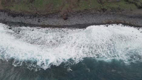 Aerial-view-of-waves-crushing-into-a-pebble-beach,-turquoise-water-and-white-foam