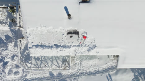 Drone-shot-above-a-showel-and-scraper-on-top-of-a-PV-system-on-a-snowy-house