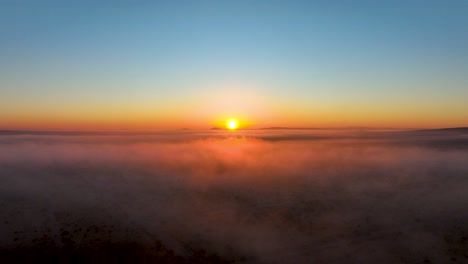 Sunrise-over-a-sea-of-clouds-with-warm-hues-gracing-the-horizon,-aerial