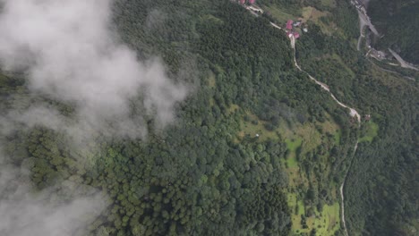 Rural-settlement-among-the-green-valley,-and-mountain,-viewed-by-drone-through-the-clouds