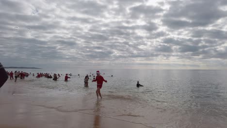 A-young-woman-dressed-as-Santa-Claus-leaving-the-cold-ocean-water-in-December