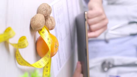 Vertical-video,-diet-specialist-using-a-table-during-a-dieting-appointment,-Walnuts-and-Tangerine-on-desk