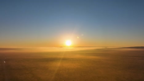 Sunrise-over-a-serene-landscape-with-light-fog,-warm-golden-tones-bathing-the-scene,-aerial