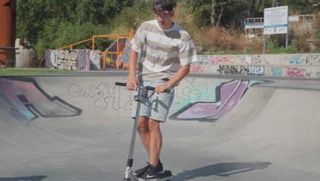 Male-on-stunt-scooter-perform-jump-and-bar-spin-trick-at-skatepark-bowl