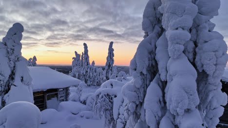 Drone-tracking-low-in-front-of-huts-and-snowy-trees-on-a-fell,-polar-night-in-Lapland