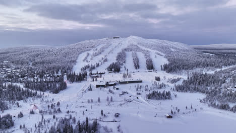Panoramic-drone-shot-circling-the-slopes-of-Iso-Syote,-winter-sunrise-in-Finland