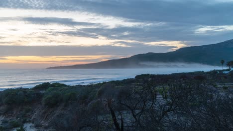 Ocean-coastline-with-sunset-sky-and-light-mist,-time-lapse-view