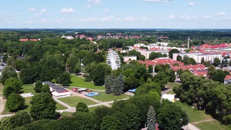 Cozy-town-of-Gizycko-with-Ferris-wheel-surrounded-by-green-forest,-aerial-view