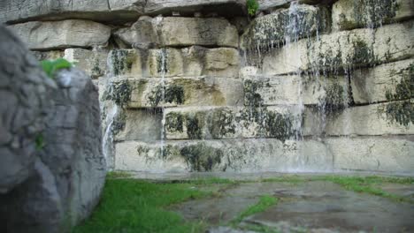 Low-Dolly-Out-Shot-of-a-Waterfall-with-a-Decorative-Stone-Wall-in-a-Garden