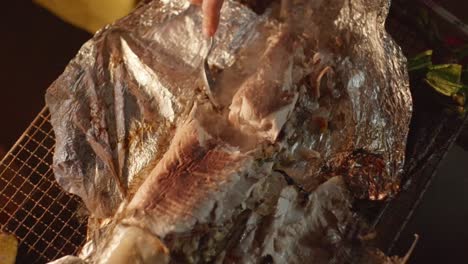 Freshly-barbecue-baked-fish-on-foil-broken-in-half-using-spoon-by-hand,-filmed-as-closeup-in-slow-motion-style