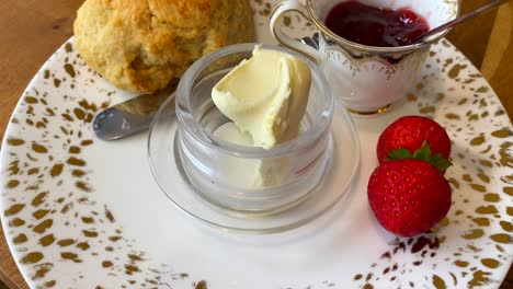 Authentic-British-scone-with-strawberry-jam,-clotted-cream-and-fresh-strawberries-with-a-cup-of-tea-in-England,-traditional-breakfast-tea-time-sweet-dessert-in-United-Kingdom,-4K-shot