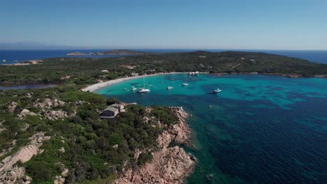 aerial-sideways-shot-panoramic-view-of-protected-area-of-Sardinia,Italy-with-boats-anchored-off-coast-and-people-enjoying-sun-during-holidays