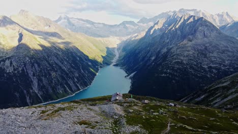 Downward-drone-shot-beautiful-scenic-view-of-European-hut-named-"Olpererhütte"-in-Austrian-Alps-in-summer-with-the-Schlegeis-Stausee-below