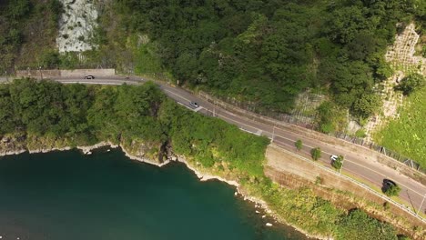 Aerial-top-down-shot-of-cars-on-road-near-river-in-Wulai-Mountains-at-sunny-day,-Taiwan---Tourism-in-village-with-parking-buses