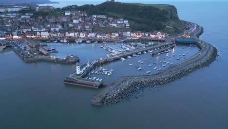 Aerial-backward-shot-of-Scarborough-Harbour-with-boats-on-ocean-during-sunset-in-December-in-Scarborough,-England