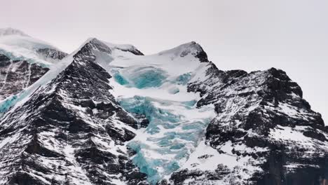 Close-up-of-dark-rugged-Switzerland-mountain-with-snow-covered-glacier-on-side