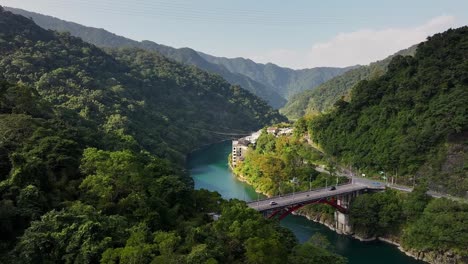Aerial-panning-shot-of-cars-on-bridge-Crossing-river-in-green-mountains-of-Wulai,-Taiwan