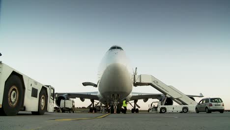 Ground-level-view-of-a-commercial-airplane-at-an-airport-during-early-evening-with-workers-and-vehicles-around