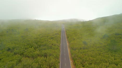 Aerial-birds-eye-shot-of-cars-on-asphalt-road-in-green-landscape-of-Madeira-during-foggy-day-on-island