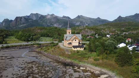 Aerial-view-of-a-Nordic-church-in-Lofoten,-Norway,-framed-by-majestic-mountains