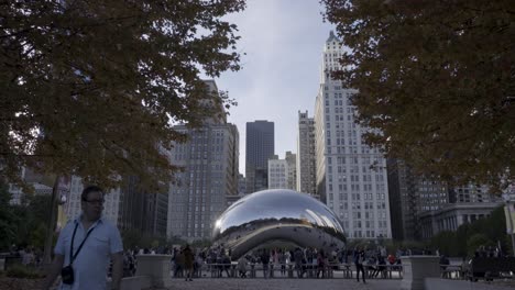Crowds-gather-around-the-reflective-Cloud-Gate-sculpture-in-Chicago's-Millennium-Park,-with-autumn-leaves-and-city-skyline