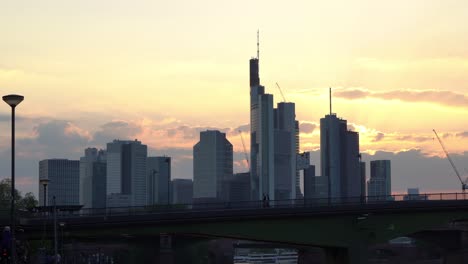 Sunset-over-Frankfurt-skyline-with-silhouettes-of-skyscrapers-and-a-bridge,-warm-glow-of-the-evening-sky