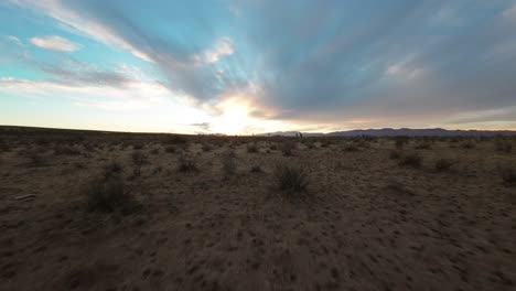 Flug-Durch-Ausgedehnte-Wüstenlandschaft-Bei-Sonnenuntergang-Mit-Dynamischem-Himmel-Und-Fernen-Bergen