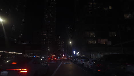 POV-Fahraufnahme-Zwischen-Beleuchteten-Wolkenkratzern-Von-Manhattan,-Nachts-In-New-York