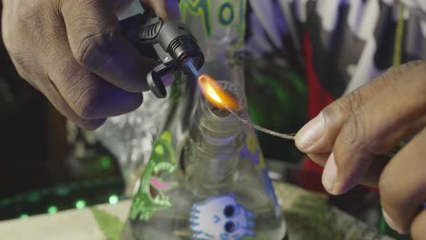 a-black-mans-hand-using-a-torch-to-light-a-wick-in-preparation-of-smoking-a-water-bong-filled-with-marijuana