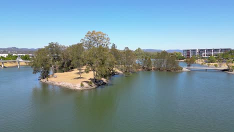 Drone-flying-westward-across-Lake-Orr-at-Varsity-Lakes-in-Queensland,-Australia-with-the-hinterland-in-the-background