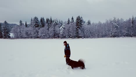Man-With-His-Alaskan-Malamute-Pet-On-Snowy-Landscape-In-Norway---Wide