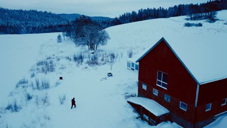 Aerial-View-Of-A-Man-Walking-Near-Barn-House-In-Winterly-Landscape