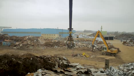 Industrial-scrapyard-with-heavy-machinery-sorting-piles-of-metal-waste-during-an-overcast-day,-creating-a-mood-of-urban-decay