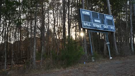 Charlotte,-North-Carolina,-United-States---14-January-2024:-Timelapse-sunset-through-the-trees-looking-at-an-old-baseball-scoreboard